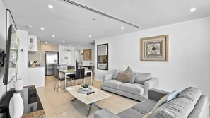 A modern living room with a grey sofa, a coffee table, and a dining area with a table and chairs. - Esplanade Soul Apartment 402 (Surfers Paradise)