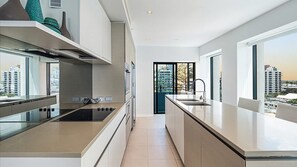 A modern kitchen with a central island, a built-in oven, and a view of the cityscape through large windows. - Esplanade Soul Apartment 605 (Surfers Paradise)