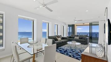 A modern living room with a glass dining table, two sofas, and a view of the ocean.