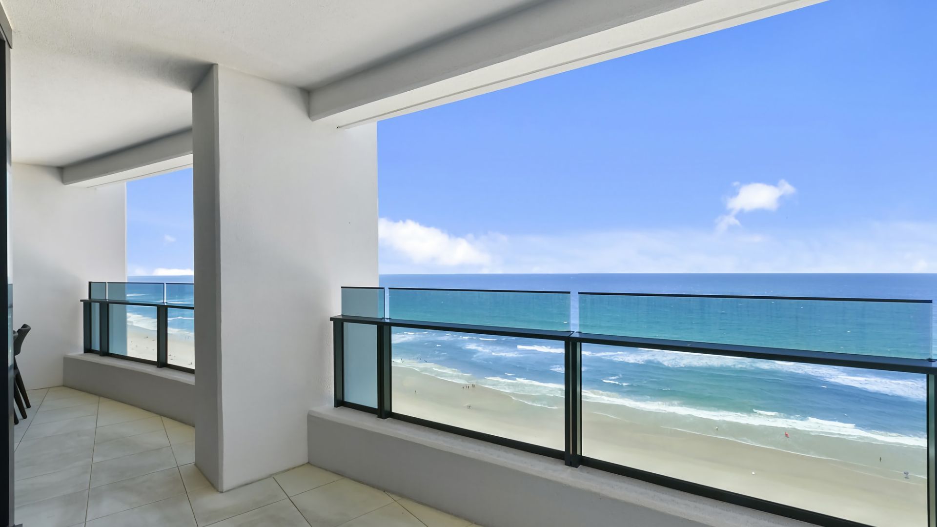 A balcony with a glass railing overlooking a beach and ocean.