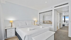 A modern hotel room with a large bed, bedside tables, a bench, a mirror, and a view of the bathroom. - Esplanade Soul Apartment 2304 (Surfers Paradise)