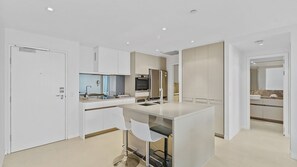 A modern kitchen with a central island, bar stools, and built-in appliances. - Esplanade Soul Apartment 2304 (Surfers Paradise)