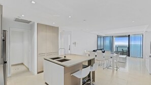 A modern kitchen with a central island, a dining area with a table and chairs, and a balcony with a view. - Esplanade Soul Apartment 2304 (Surfers Paradise)