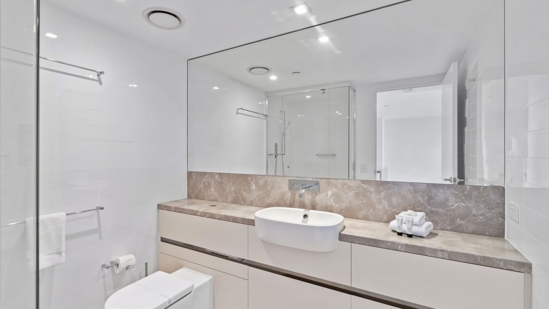 A modern bathroom with a glass shower enclosure, a white sink, and a large mirror.