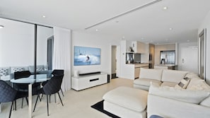 A modern living room with a dining area, a kitchen, and a large window. - Esplanade Soul Apartment 2502 (Surfers Paradise)