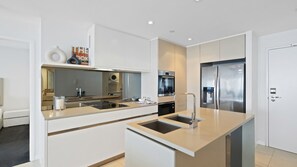 A modern kitchen with a central island, stainless steel appliances, and a built-in oven. - Esplanade Soul Apartment 2502 (Surfers Paradise)