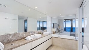 A modern bathroom with a large mirror, two sinks, a bathtub, and a view of the sea. - Esplanade Soul Apartment 3001 (Surfers Paradise)