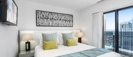 A hotel room with a large bed, two bedside tables with lamps, a city view, and a framed abstract artwork on the wall.