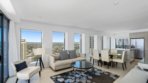 A modern living room with a sofa, a coffee table, and a dining area with chairs. Large windows provide a view of the cityscape. - Esplanade Soul Apartment 3001 (Surfers Paradise)