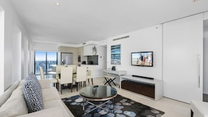A modern living room with a glass coffee table, a sofa, and a view of the city. - Esplanade Soul Apartment 3001 (Surfers Paradise)