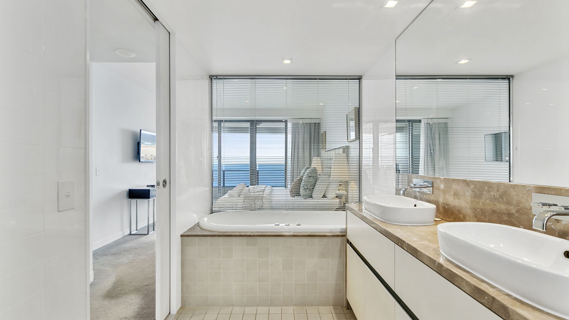 Ein modernes Badezimmer mit einem großen Spiegel, zwei Waschbecken und Meerblick durch die Fenster.