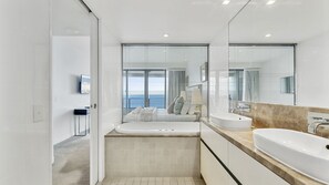 Ein modernes Badezimmer mit einem großen Spiegel, zwei Waschbecken und Meerblick durch die Fenster.