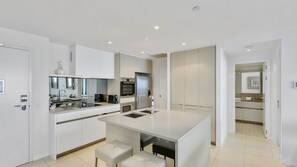 A modern kitchen with white cabinetry, a central island, and a built-in oven. - Esplanade Soul Apartment 3004 (Surfers Paradise)