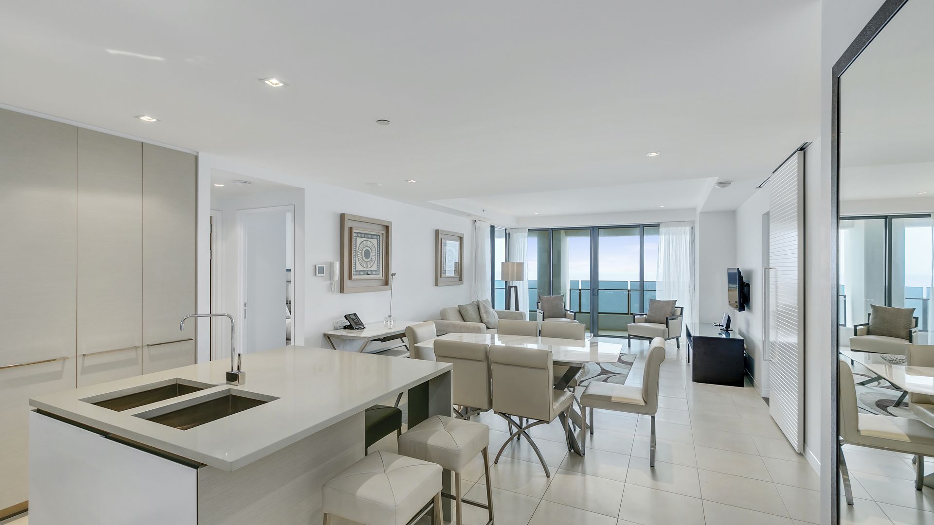 A modern hotel room with a kitchen area, dining space, and a balcony with a view.