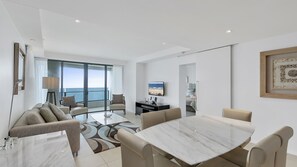 Un salon moderne doté d’une grande fenêtre, un coin repas avec une table en marbre et une chambre à coucher visible à travers une porte ouverte.