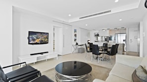 A modern living room with a flat-screen TV, a dining area with a table and chairs, and a kitchen in the background. - Esplanade Soul Apartment 5004 (Surfers Paradise)