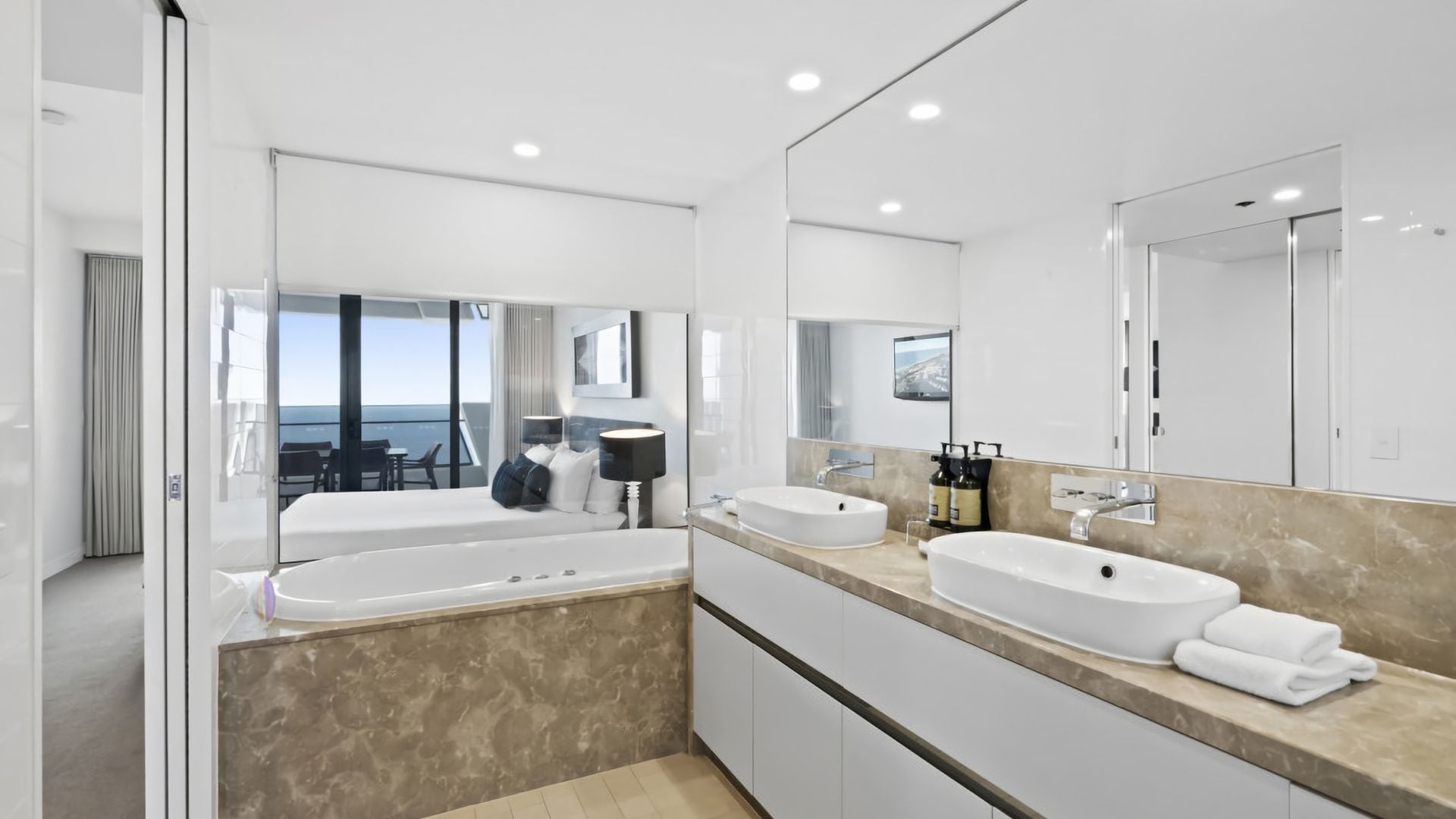 A modern bathroom with a large bathtub, two sinks, and a large mirror.