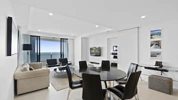 A modern living room with a round table, black chairs, a sofa, and a TV mounted on the wall.