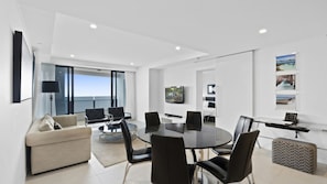 A modern living room with a round table, black chairs, a sofa, and a TV mounted on the wall. - Esplanade Soul Apartment 5004 (Surfers Paradise)
