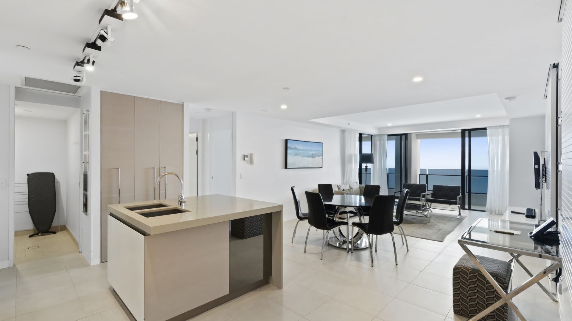 A modern kitchen with a central island, dining area with chairs, and a view of the sea through large windows.