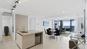 A modern kitchen with a central island, dining area with chairs, and a view of the sea through large windows.