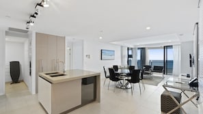 A modern kitchen with a central island, dining area with chairs, and a view of the sea through large windows. - Esplanade Soul Apartment 5004 (Surfers Paradise)