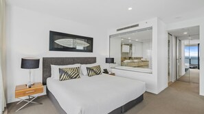 A modern hotel room with a large bed, bedside lamps, a large mirror, and a view of the sea through a glass door. - Esplanade Soul Apartment 5005 (Surfers Paradise)