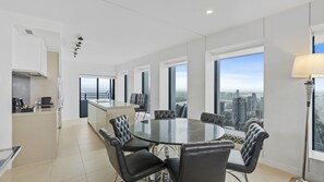 A modern kitchen with a central island, a dining area with a round table and chairs, and large windows offering a city view. - Esplanade Soul Apartment 5005 (Surfers Paradise)