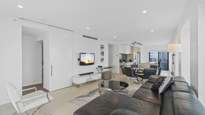 A modern living room with a black leather sofa, a glass coffee table, and a flat-screen TV mounted on the wall. - Esplanade Soul Apartment 5005 (Surfers Paradise)
