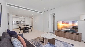 A modern living room with a flat-screen TV, a sofa, a coffee table, and a dining area with chairs. - Esplanade Soul Apartment 6102 (Surfers Paradise)