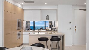 A modern kitchen with a large island, bar stools, and a view of the sea. - Esplanade Soul Apartment 6102 (Surfers Paradise)