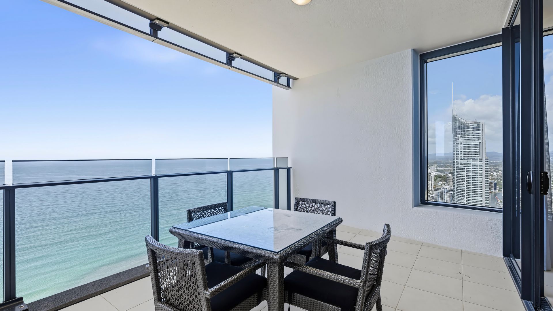 Un balcone con tavolo e sedie, con vista su un corpo d'acqua e sullo skyline della città.