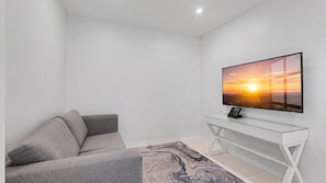 A modern living room with a flat-screen TV mounted on a white console, a grey sofa, and a marble-patterned rug. - Esplanade Soul Apartment 6102 (Surfers Paradise)