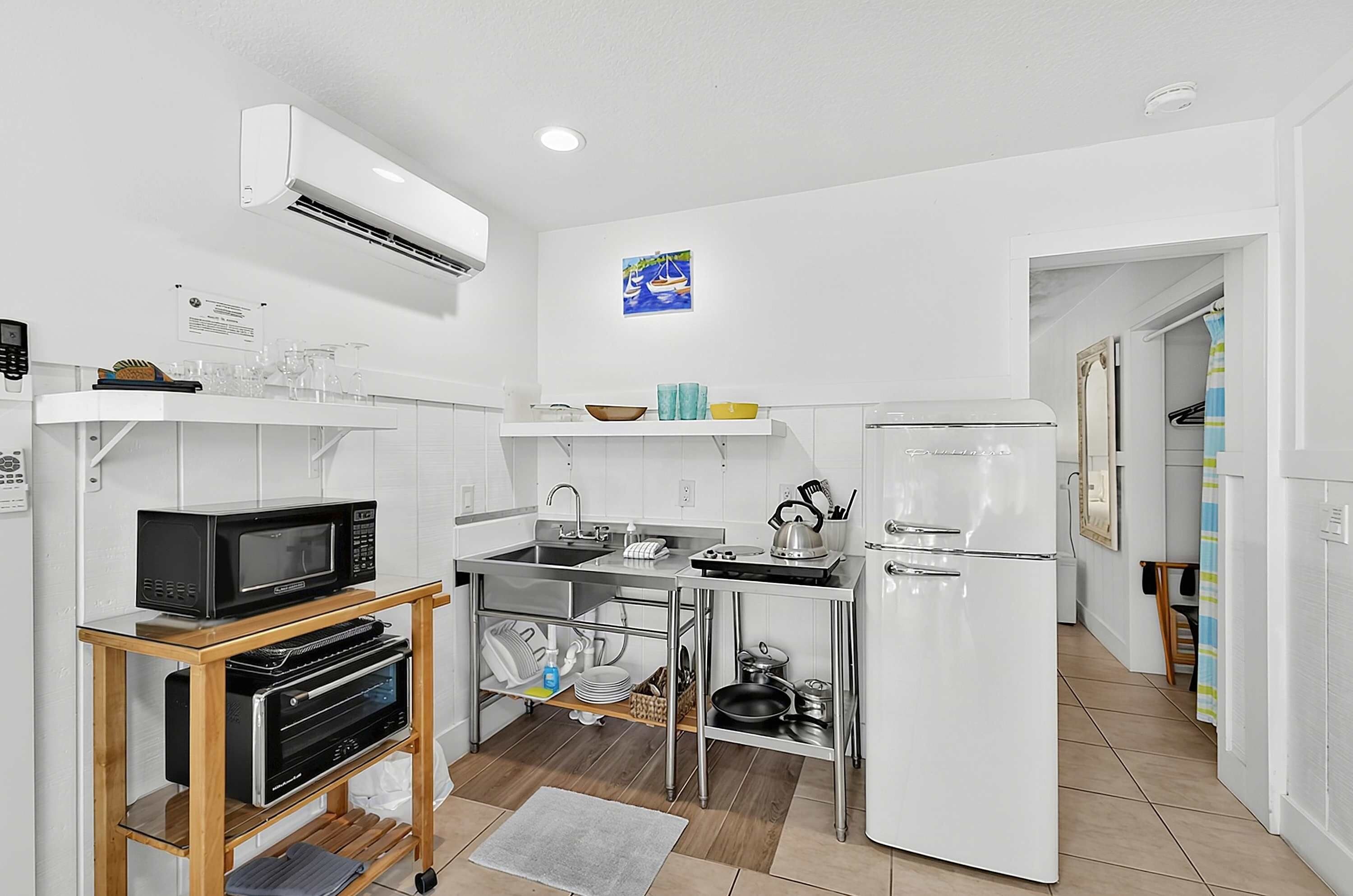 A compact kitchen with a microwave, oven, and refrigerator. There is a small sink and a kettle.