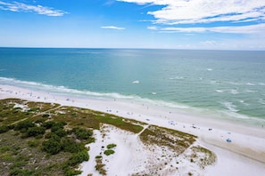 Uma praia com vista clara do oceano, faixa de areia e vegetação rasteira.