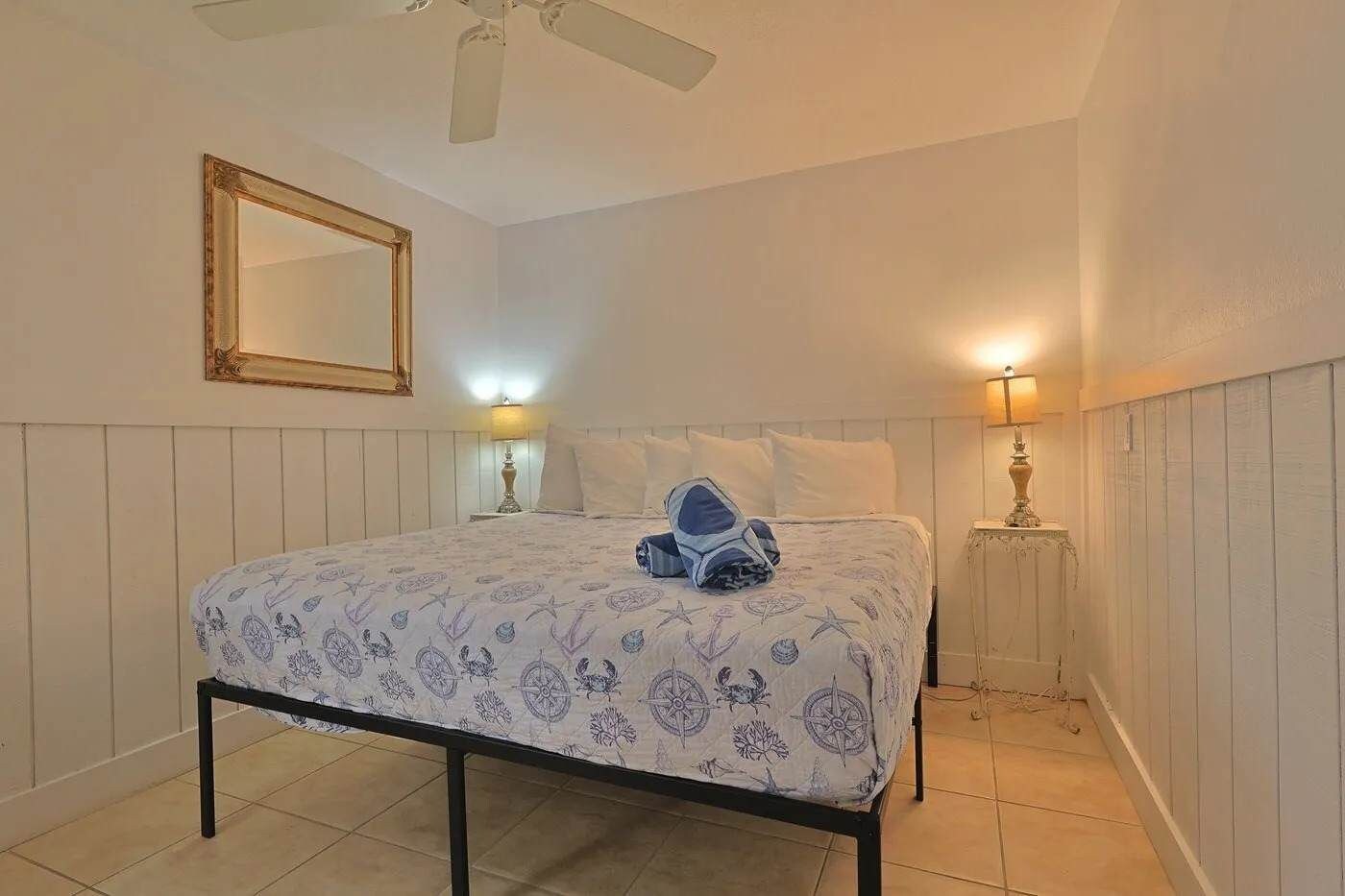 A bedroom with a bed, a ceiling fan, a mirror, and two bedside lamps.