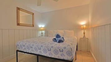 Een slaapkamer met een bed, een plafondventilator, een spiegel en twee bedlampjes.