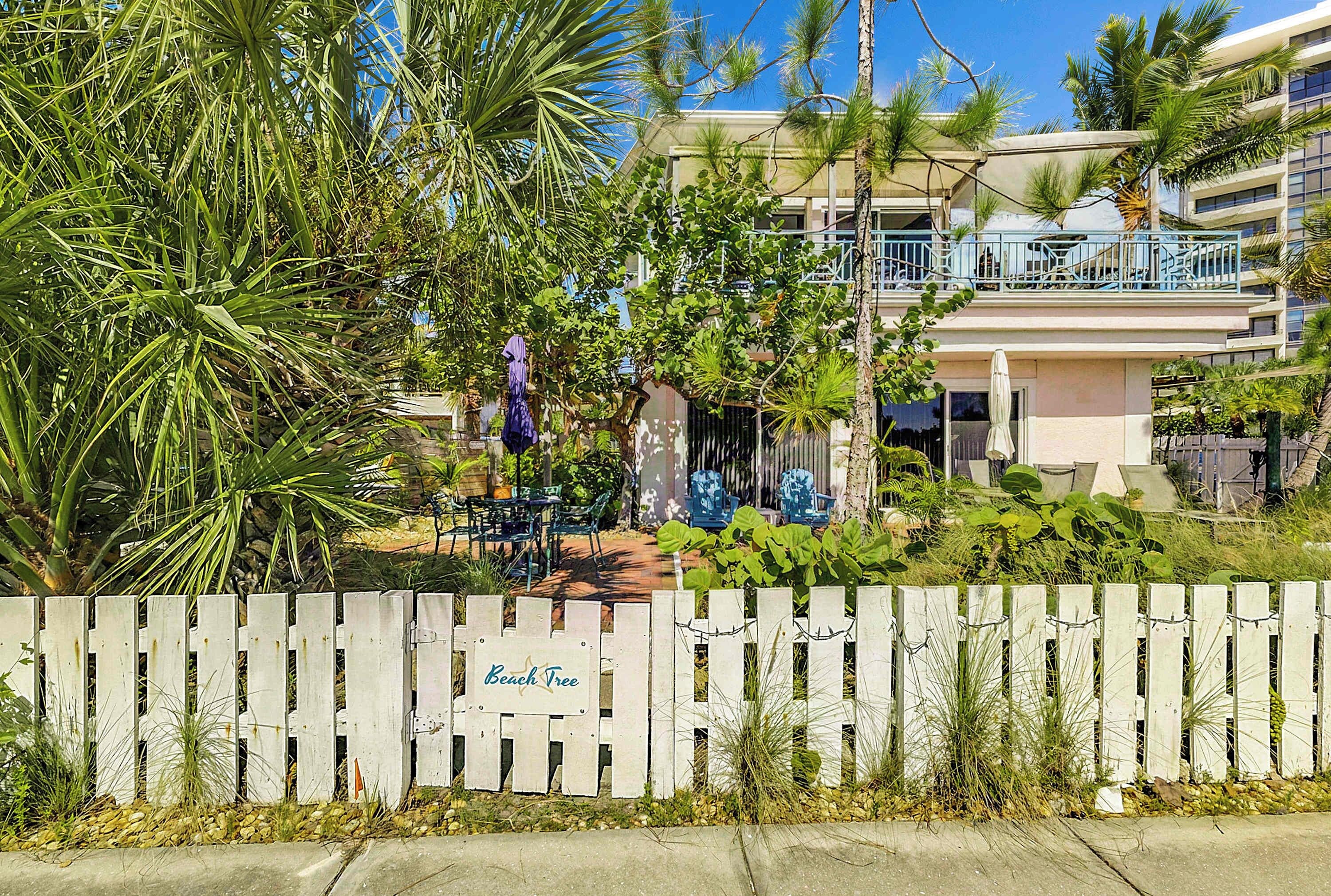 A fenced area with a sign reading 'Beach Tree' and a building with balconies in the background.