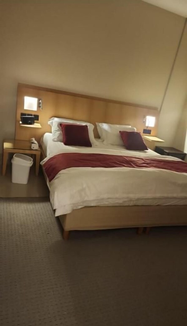 Una habitación de hotel con una cama grande, dos mesitas de noche y un cubo de basura.