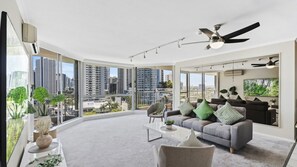 A modern living room with a large window, a ceiling fan, and a city view. - Moorings Apartment 39 (Surfers Paradise)