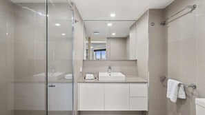 A modern bathroom with a glass shower enclosure, a white sink, and a towel rack. - Moroccan Apartment 143 (Surfers Paradise)