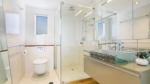 Ein modernes Badezimmer mit einer Duschkabine aus Glas, einer Toilette und einem Waschtisch mit Becken und Spiegel.