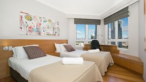 Ein Hotelzimmer mit zwei Betten, einem Schreibtisch und einem großen Fenster mit Blick auf die Stadt.