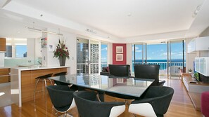 A modern interior with a glass dining table, black and white chairs, a kitchen area, and a balcony with a view. - Moroccan Apartment 269 (Surfers Paradise)
