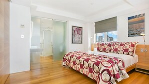 Un dormitorio moderno con una cama grande, cabina de ducha de vidrio y vistas a la ciudad.