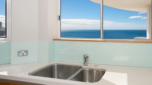 A kitchen with a double stainless steel sink, a window with a view of the sea, and a power outlet on the wall. - Moroccan Apartment 269 (Surfers Paradise)