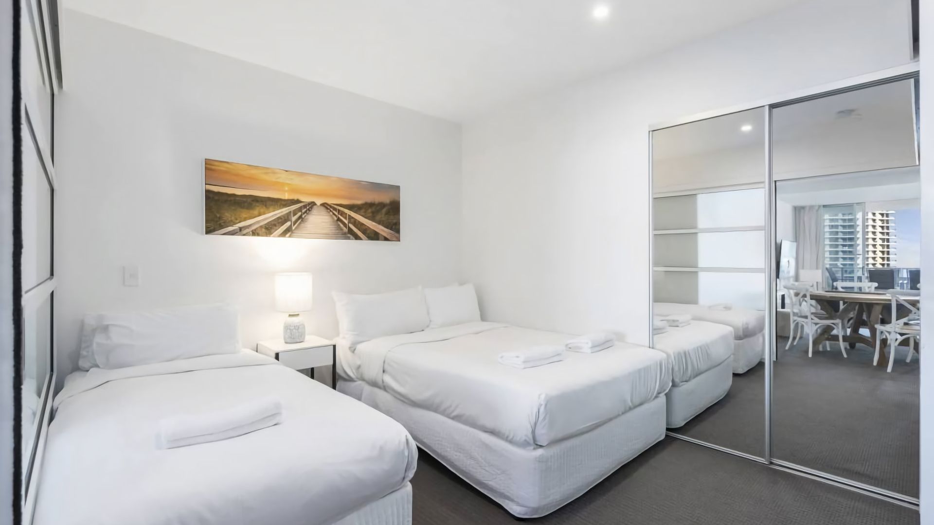 A hotel room with two beds, a desk, and a view of the city through a glass door.