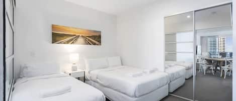 A hotel room with two beds, a desk, and a view of the city through a glass door.