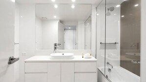 Une salle de bain moderne avec un grand miroir, un lavabo rond et une douche séparée par une paroi de verre.