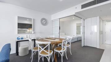 A modern, well-lit room with a round wooden table surrounded by white chairs, a large mirror, and a clock on the wall.